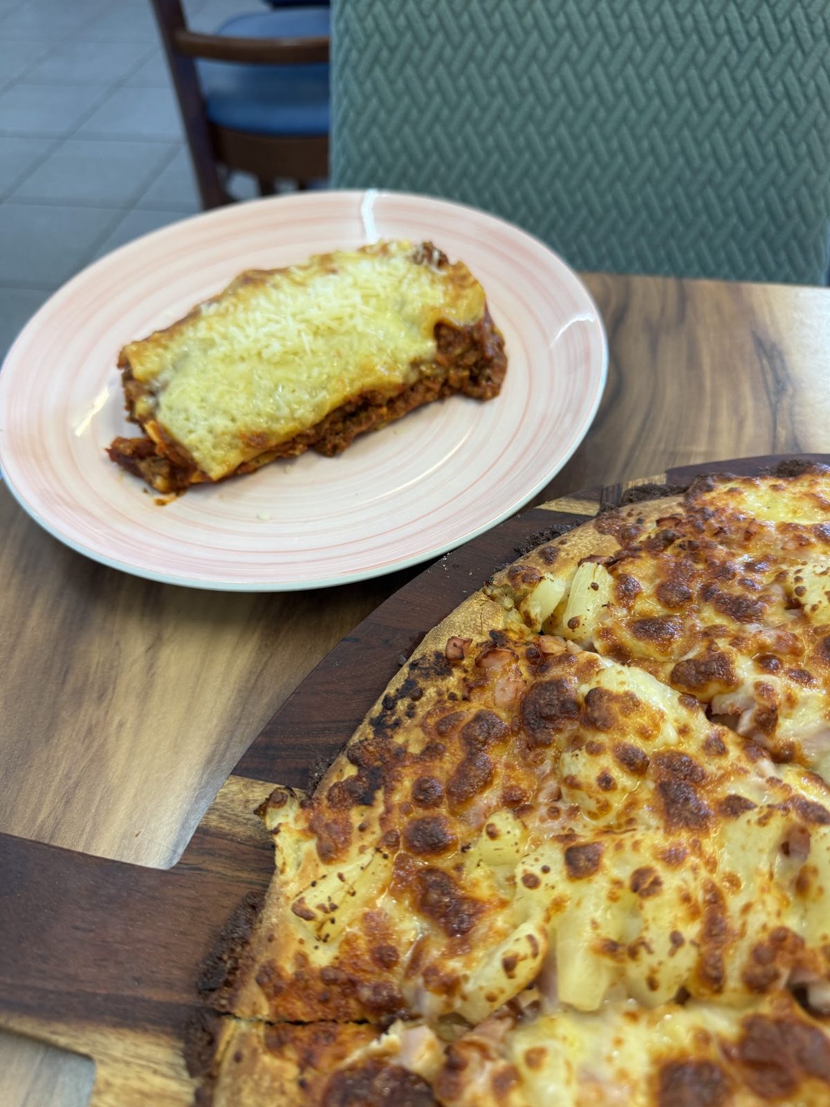 A serve of lasagne next to a ham and pineapple pizza